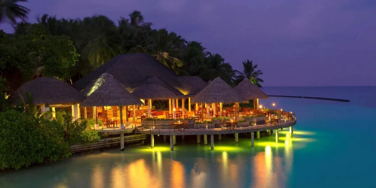 Thatched overwater restaurant glowing with lights at dusk