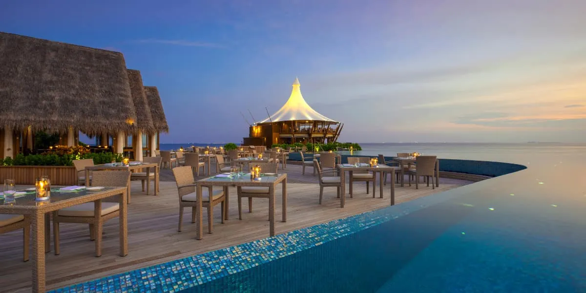 Dining tables beside a pool at dusk with The Lighthouse in the distance