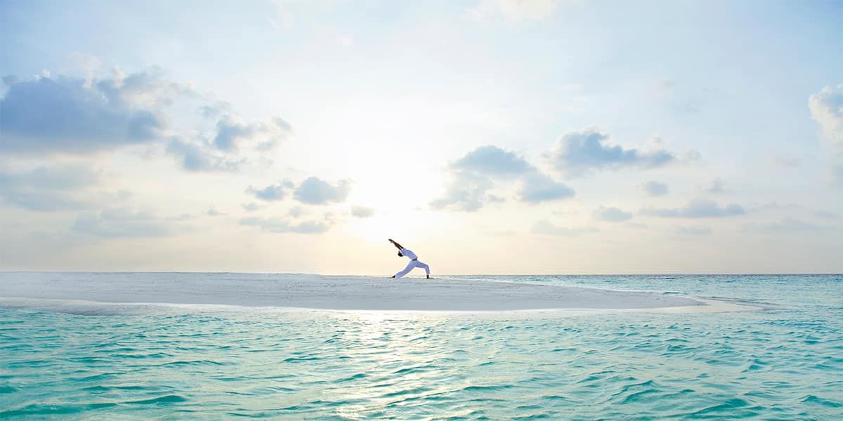 Person in a yoga pose on a sandbank at sunrise