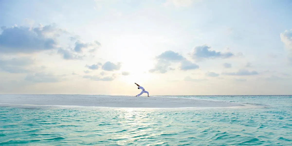 Person in a yoga pose on a sandbank at sunrise