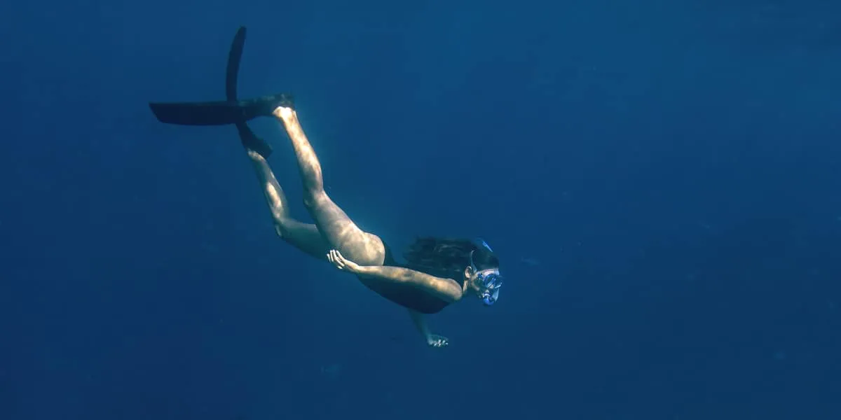 Freediver swimming down through deep blue water