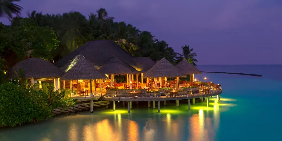 Thatched overwater restaurant glowing with lights at dusk