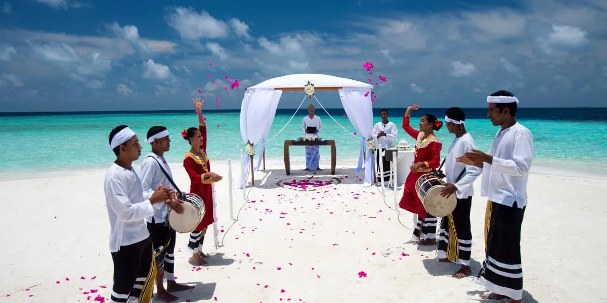 Drummers and dancers in traditional dress at a beach wedding with a white canopy