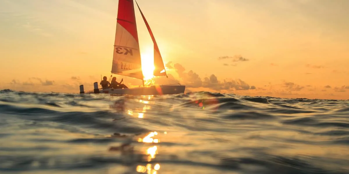 Catamaran with a red sail on the sea at sunset