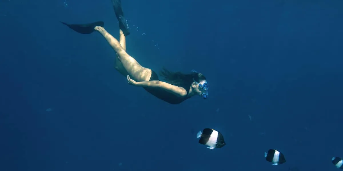 Freediver swimming down towards fish in deep blue water