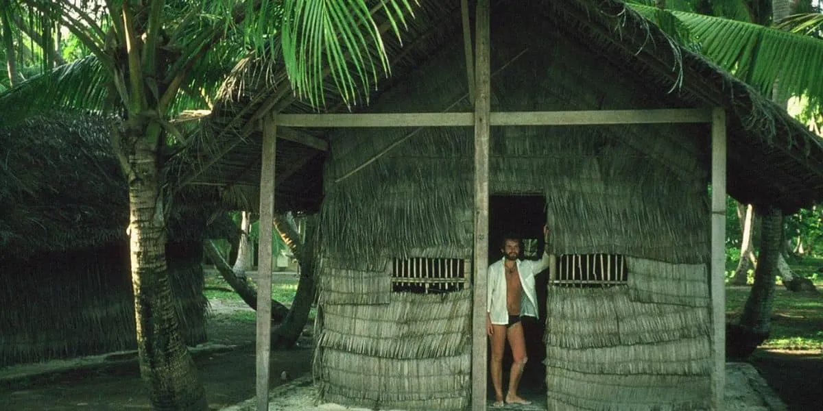 Man standing in the doorway of a traditional thatched hut