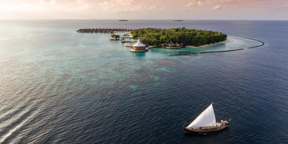 Aerial view of Baros island and water villas with a dhoni sailing nearby