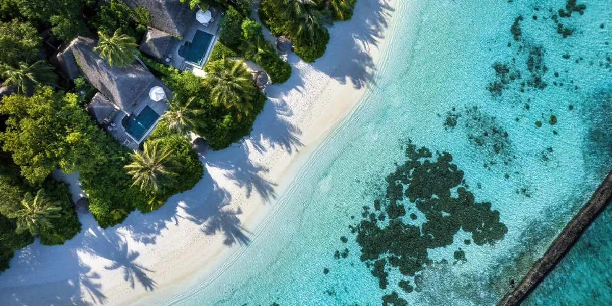 Aerial view of beach villas, palms and white sand beside a turquoise lagoon