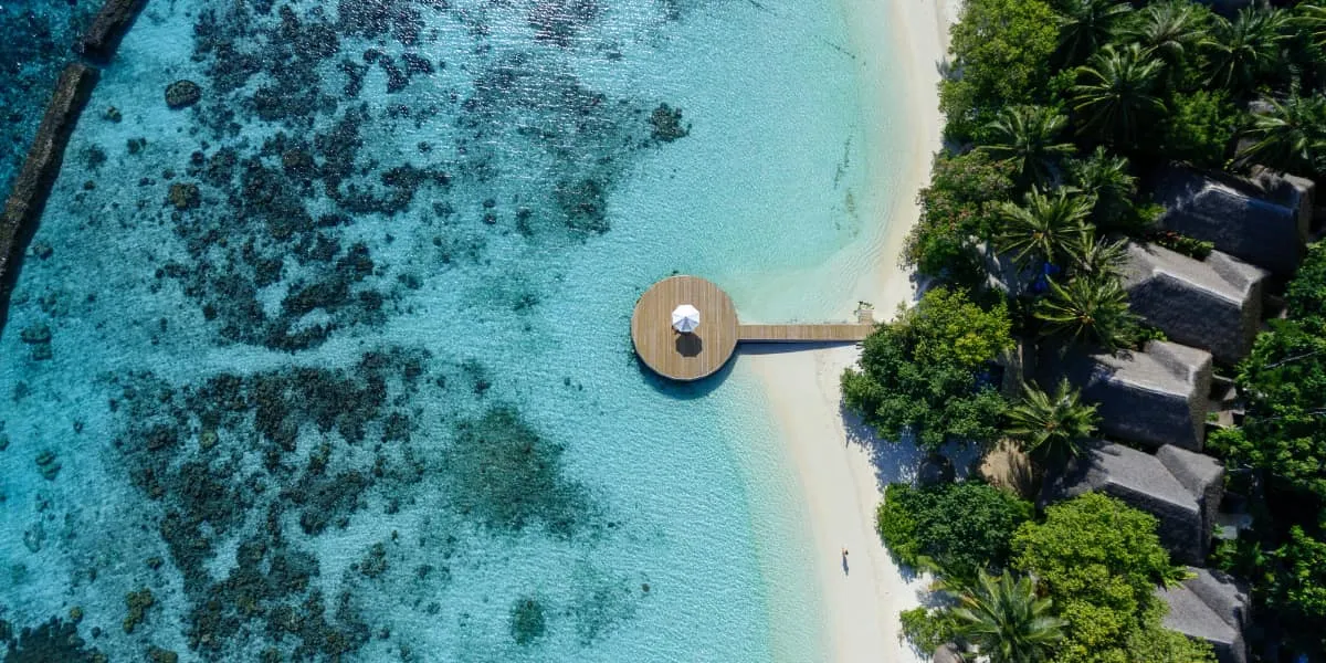 Aerial view of a round jetty platform over the reef beside a palm-fringed beach