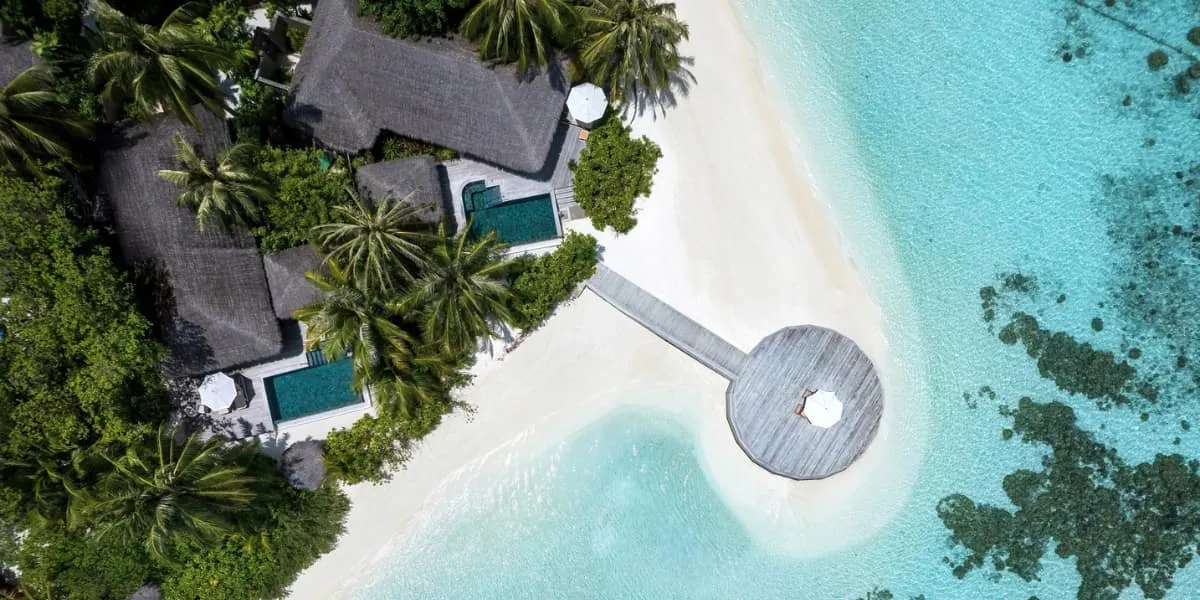 Aerial view of villas with private pools and a round jetty on the beach