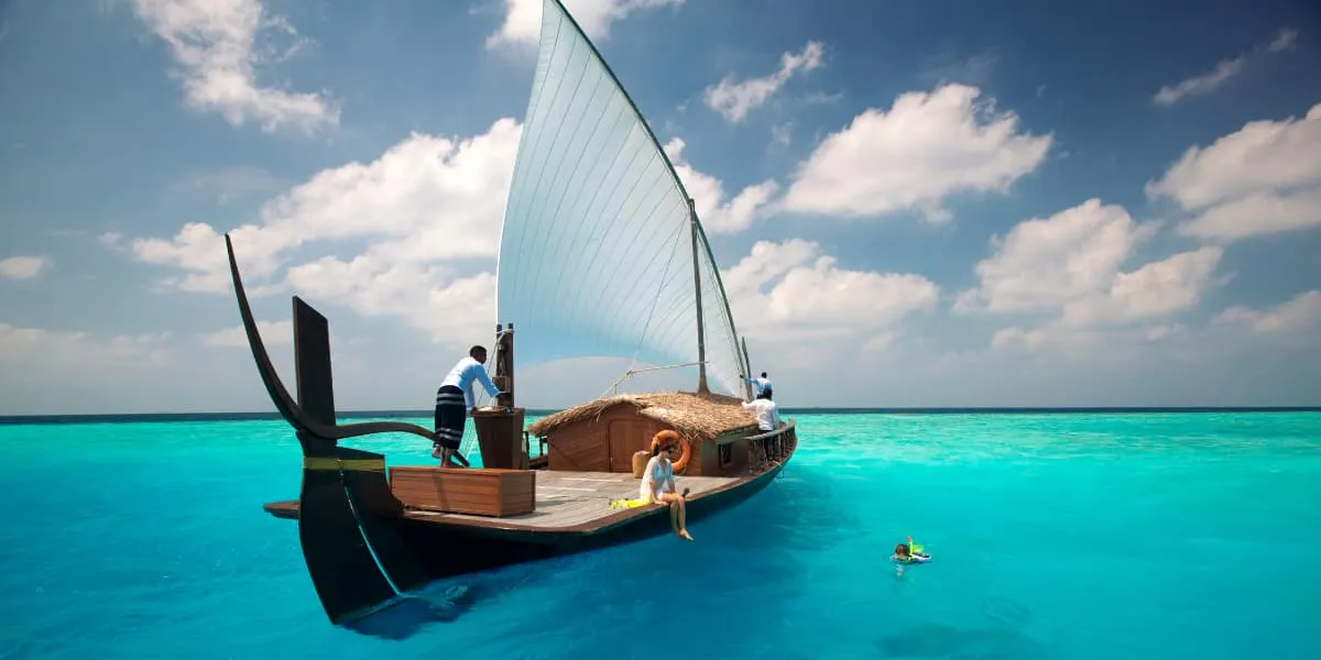 Guests aboard a traditional dhoni with its sail up on a turquoise lagoon