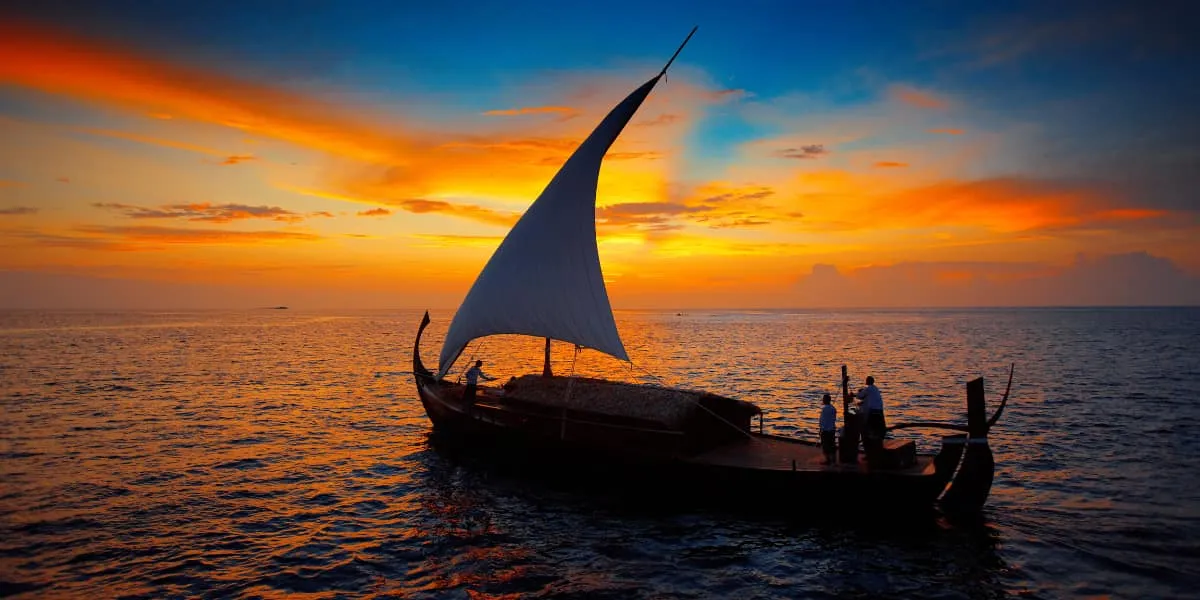 Traditional dhoni sailing at sunset under an orange sky