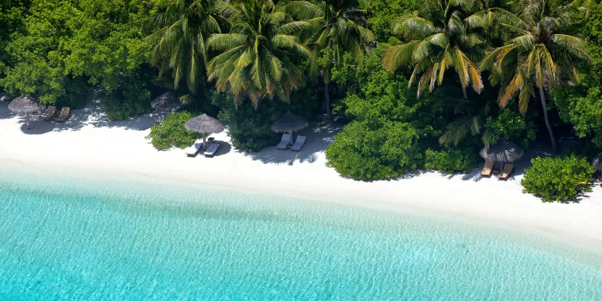 Aerial view of a white sand beach lined with palms and a clear turquoise lagoon