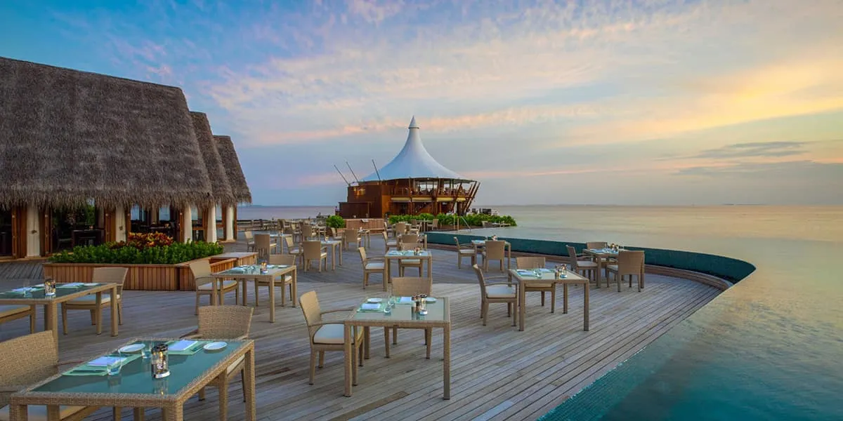 Outdoor restaurant deck with tables over the water at Baros at dusk