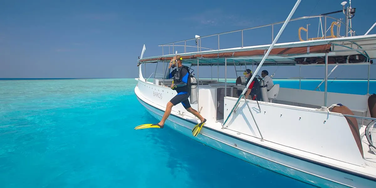 Diver in fins stepping off the back of a dive boat into turquoise water