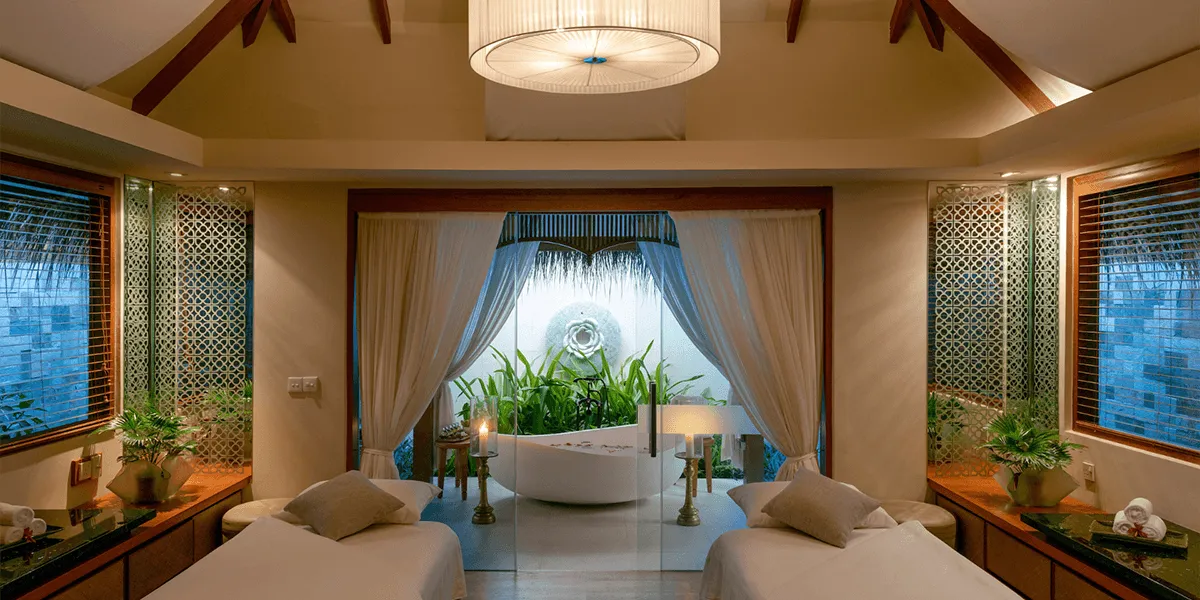 Spa treatment room with twin massage beds, a bathtub and tropical plants