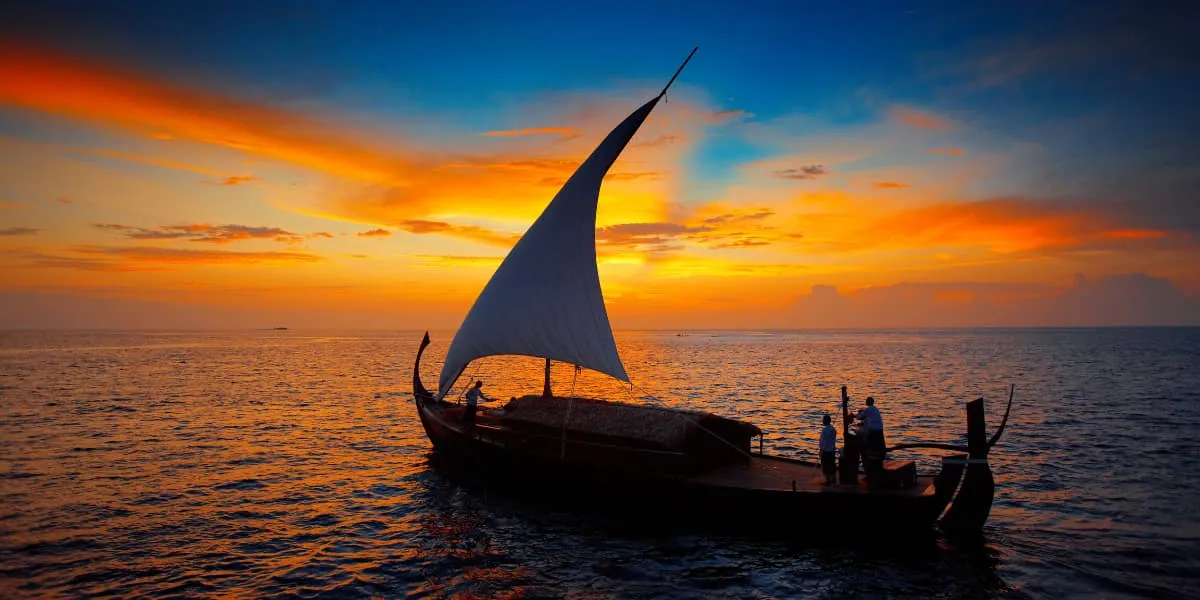 Traditional dhoni sailing at sunset under an orange sky