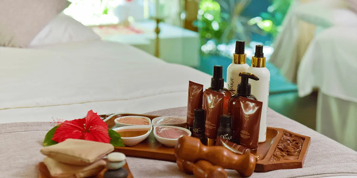 Spa tray with massage oils, balms, hibiscus and wooden tools on a treatment bed