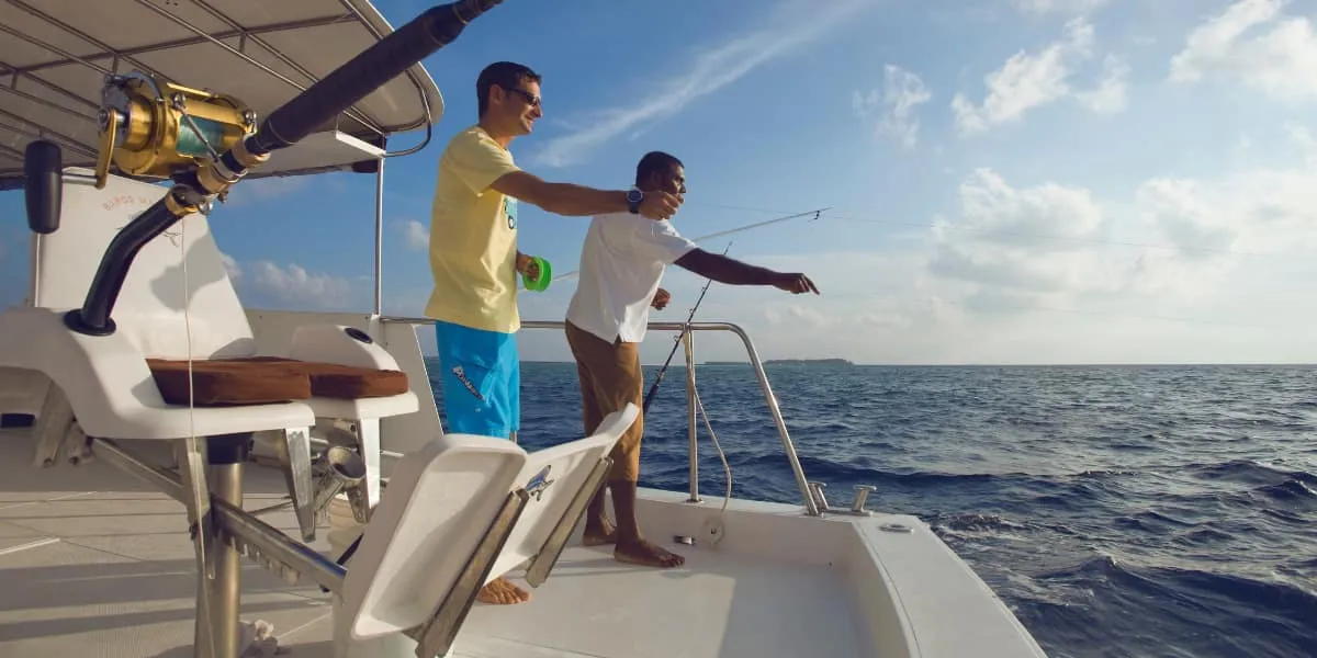 Two men fishing with rods from the deck of a boat at sea