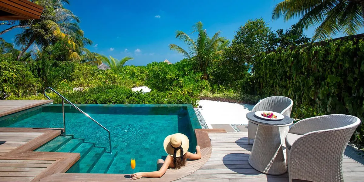 Woman in a sun hat relaxing at the edge of a villa pool with a drink