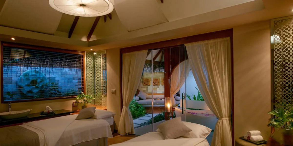 Candlelit spa treatment room with massage beds and curtains