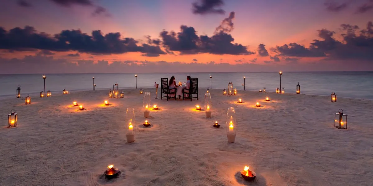 Couple dining on a sandbank surrounded by candles at sunset