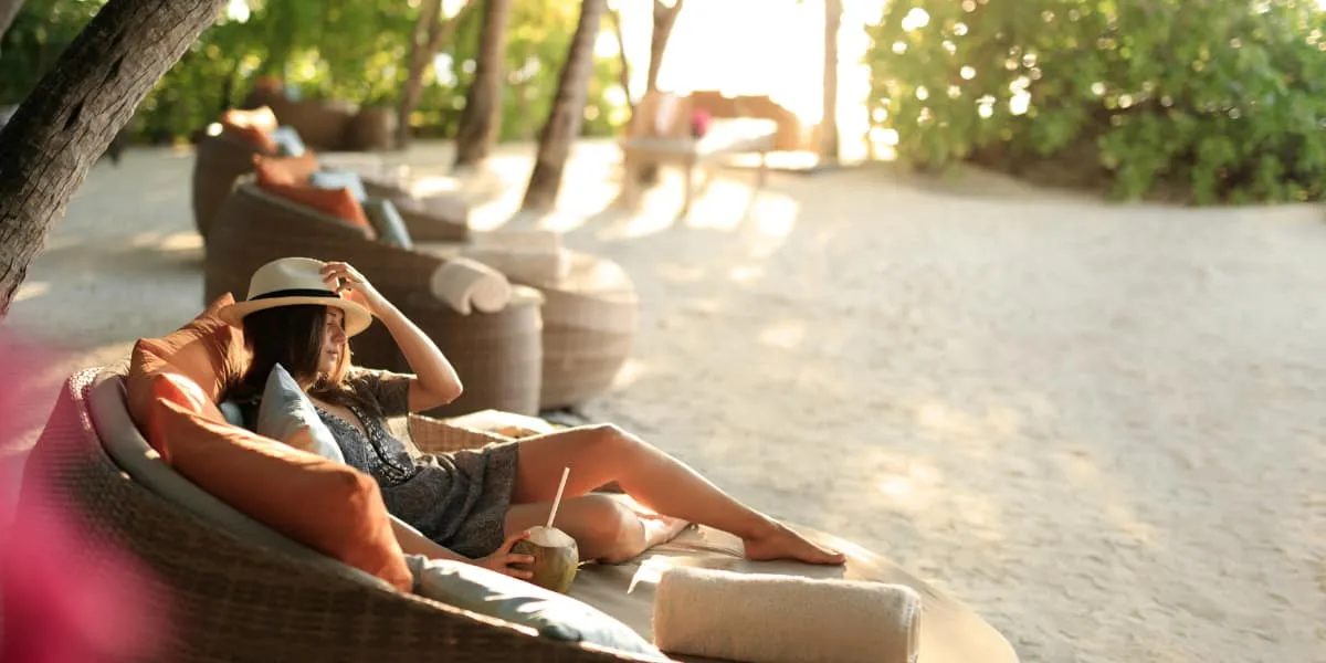 Woman relaxing in a round lounge chair on a shaded sandy beach