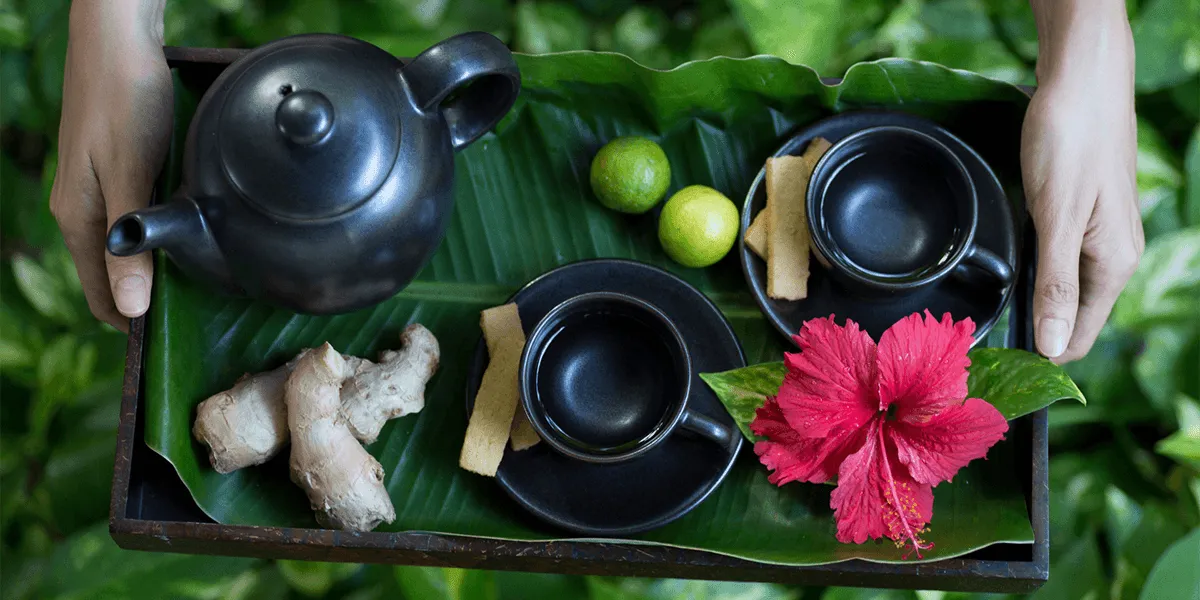 Tray of black teapot and cups with ginger, limes and a hibiscus flower