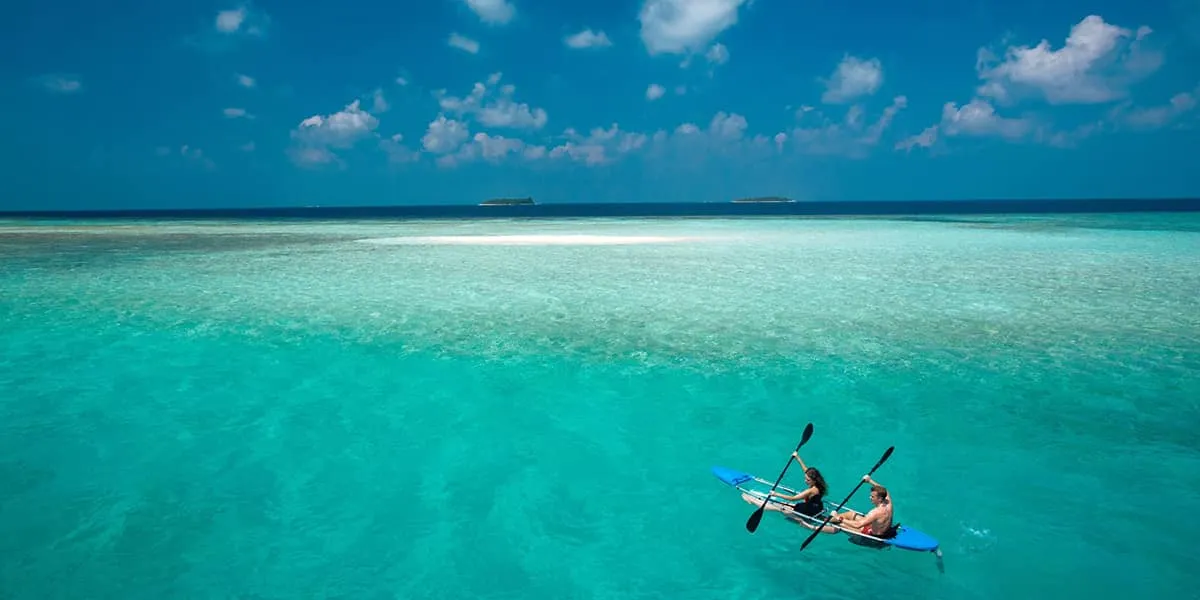 Couple paddling a clear kayak across a turquoise lagoon