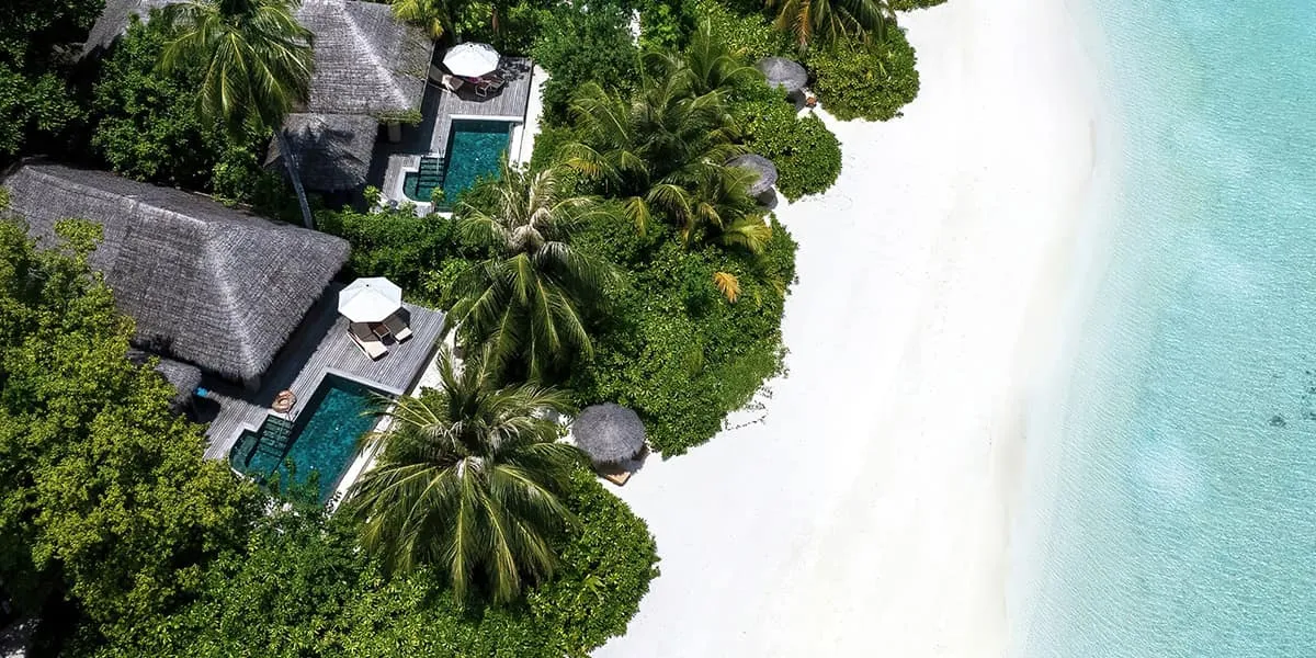 Aerial view of pool villas among palms beside a white sand beach