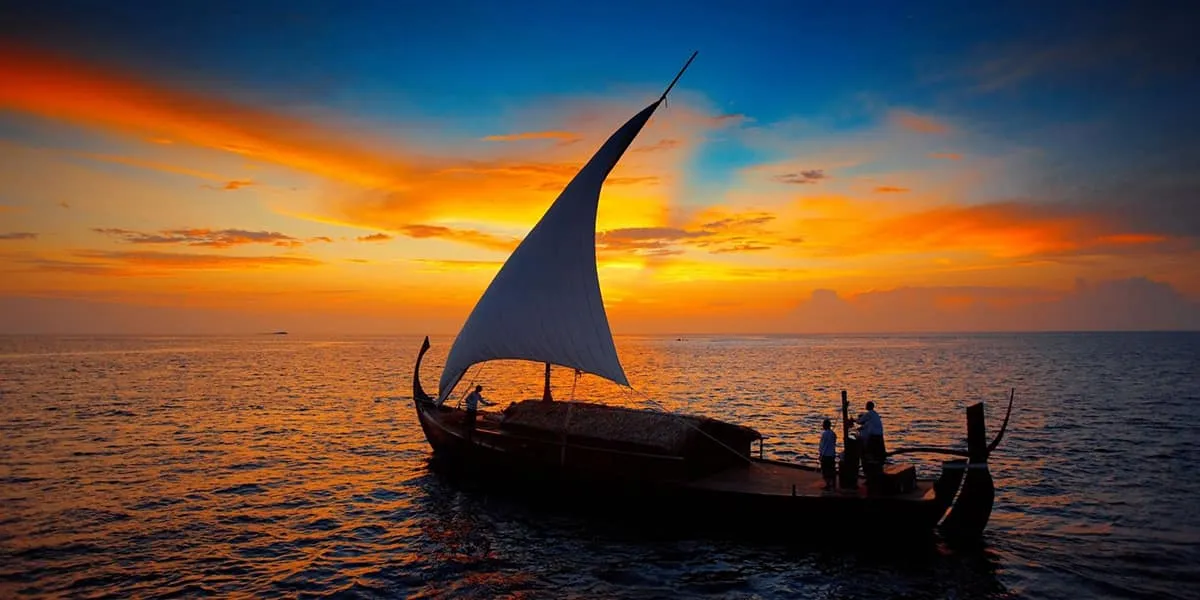 Traditional dhoni sailing at sunset under an orange sky