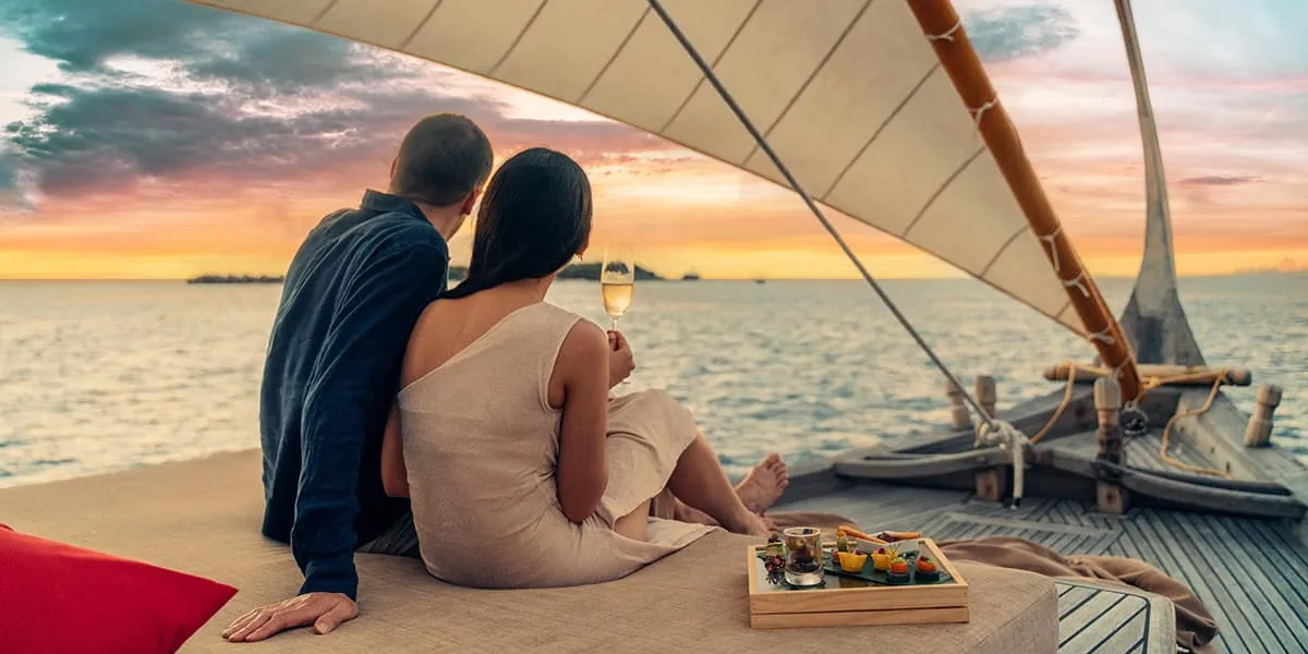 Couple with champagne and snacks relaxing on the deck of a sailing dhoni at sunset