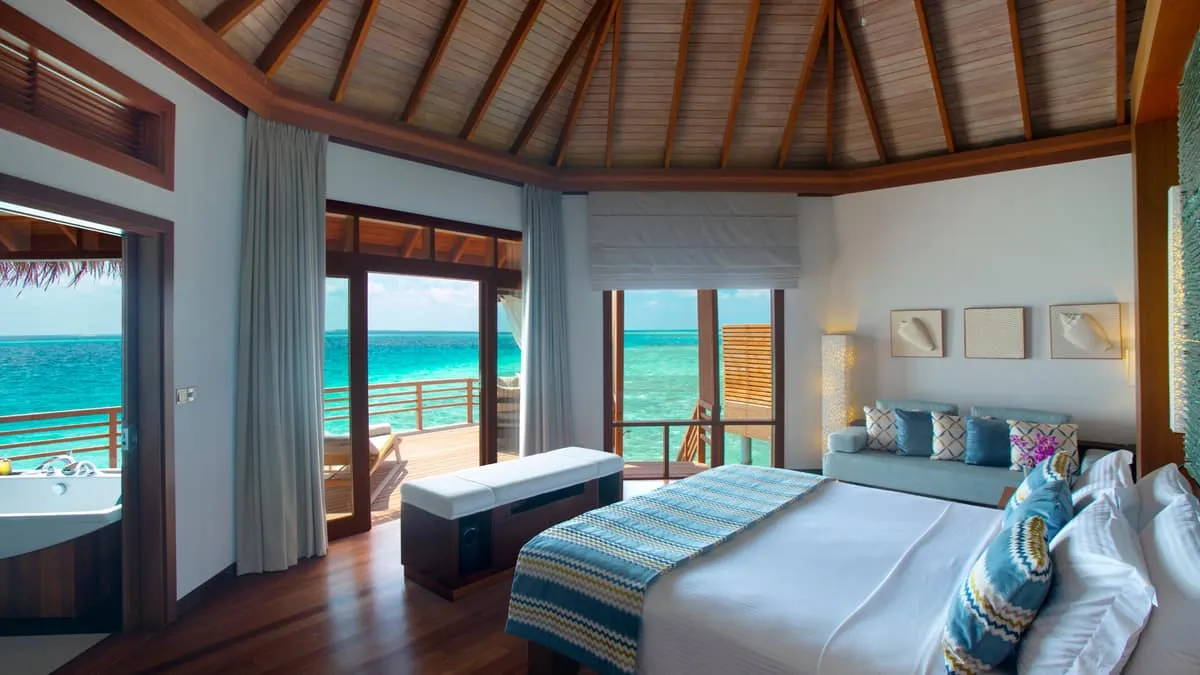 Water villa bedroom with a wooden ceiling and doors opening onto the lagoon