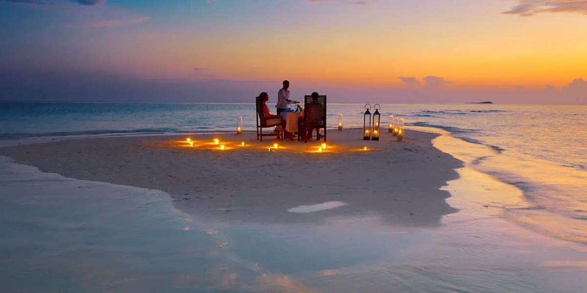 Couple dining at a candlelit table on a sandbank at sunset