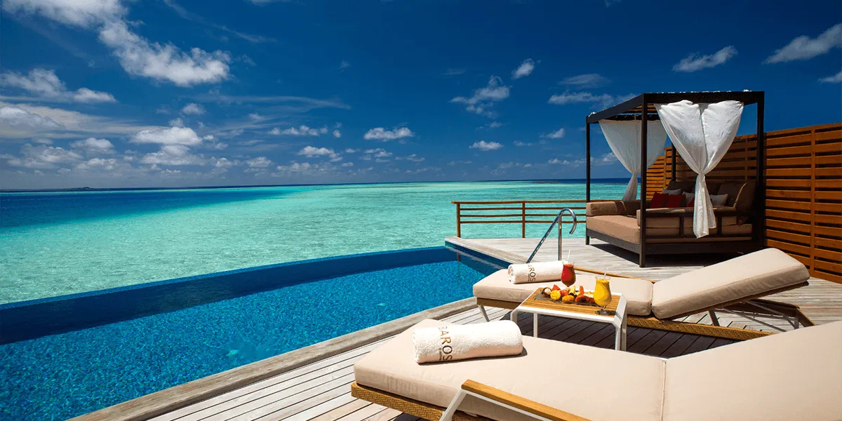 Water villa deck with a daybed, sun loungers and infinity pool facing the lagoon