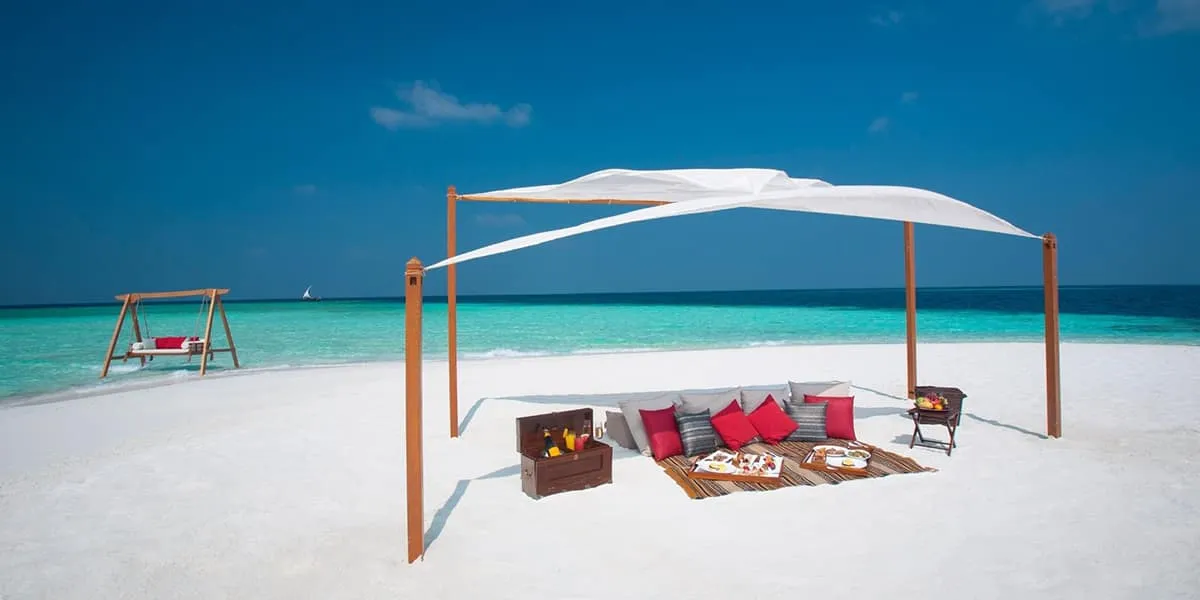 Sandbank picnic with cushions under a white shade canopy and a swing nearby