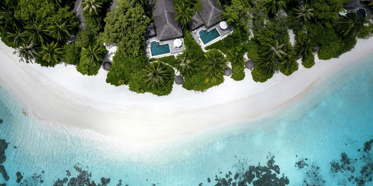 Aerial view of pool villas among palms above a white sand beach