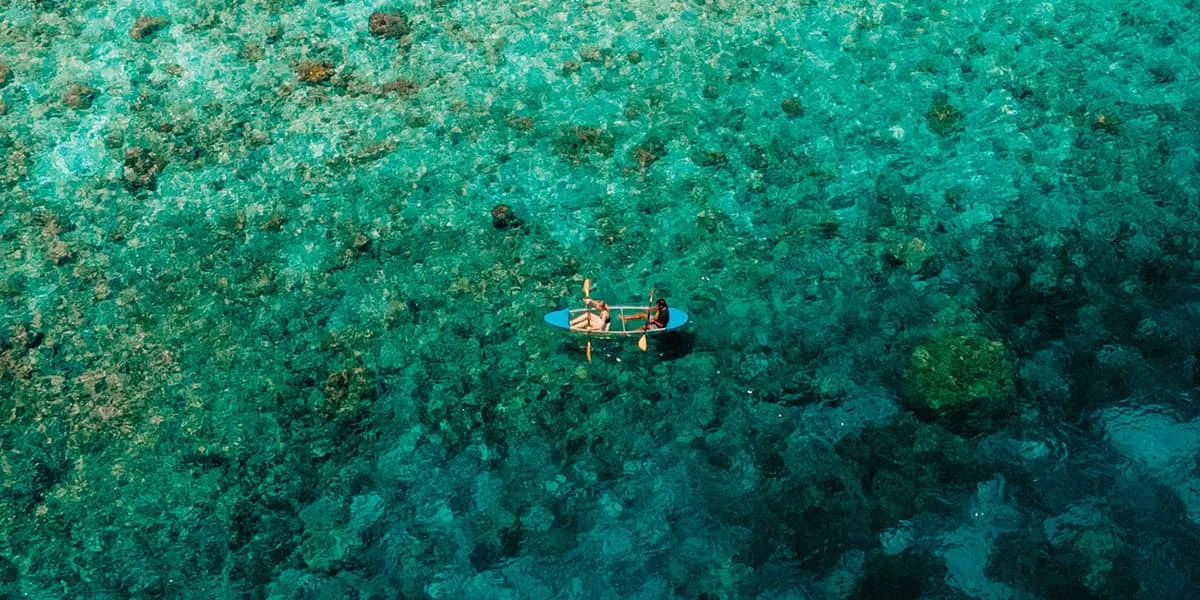 Aerial view of two people paddling a kayak over a coral reef