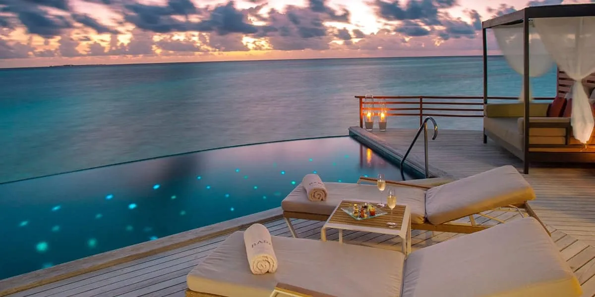 Water villa deck with sun loungers and a pool facing the sea at sunset