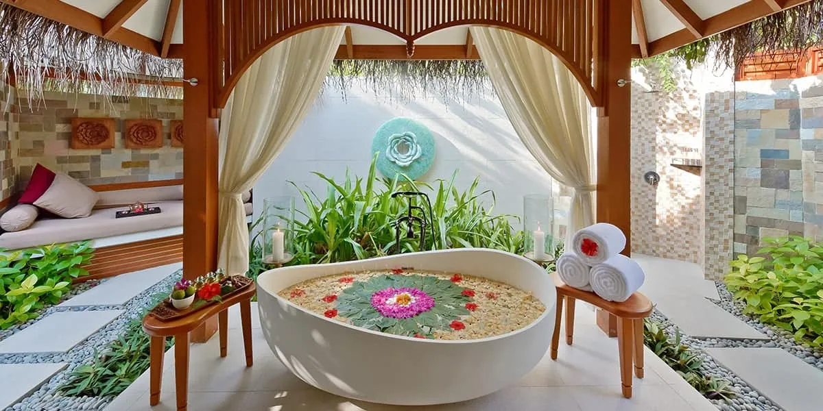 Open-air spa pavilion with a flower-filled bathtub and tropical plants