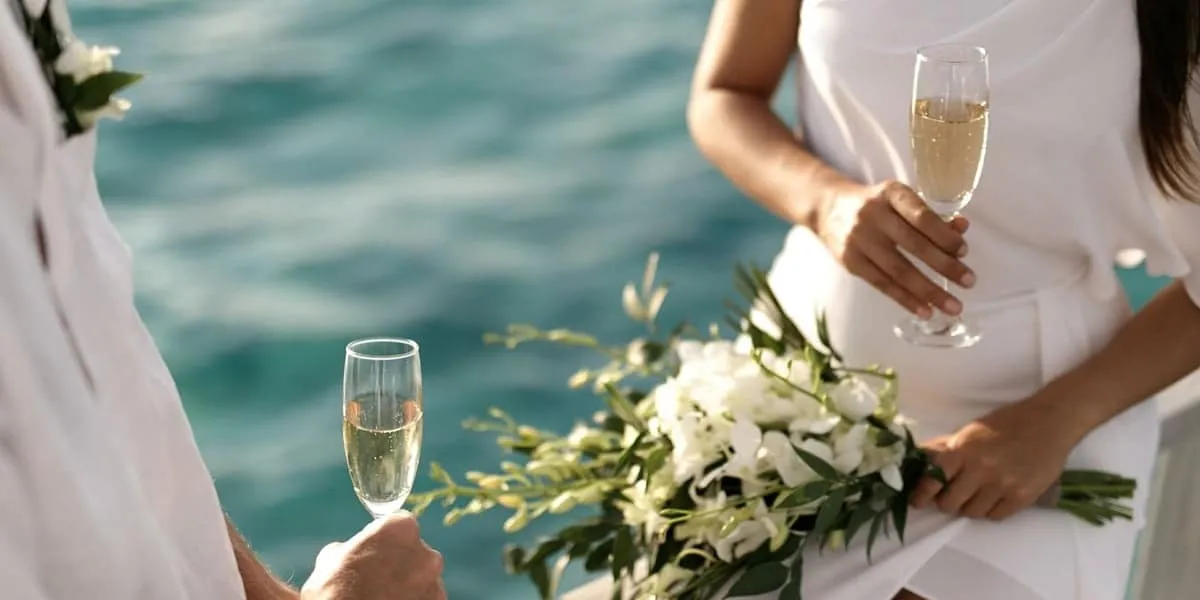 Couple holding champagne glasses and a white bouquet by the sea