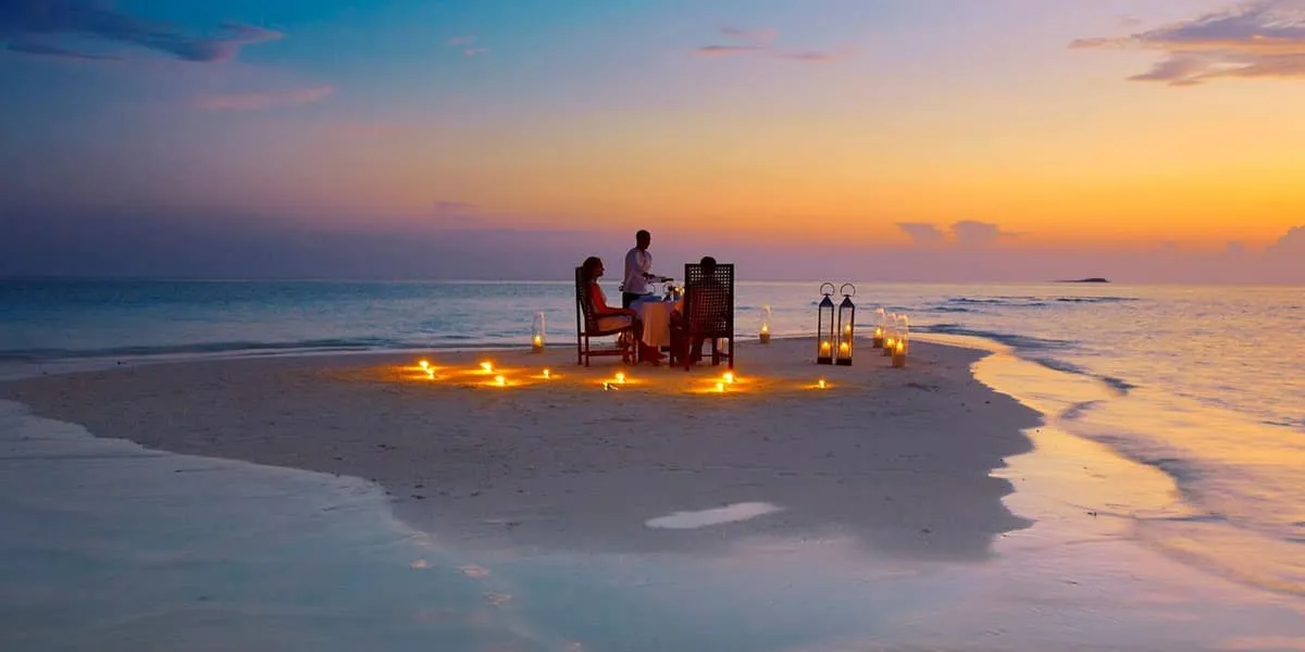 Couple dining at a candlelit table on a sandbank at sunset