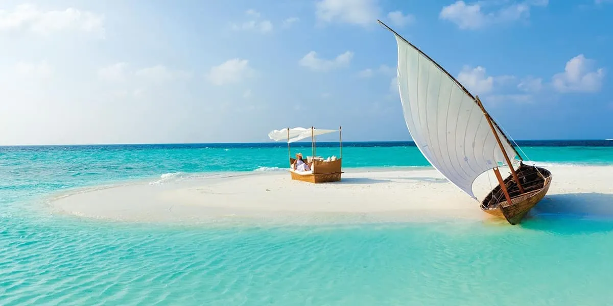 Picnic under a canopy on a sandbank with a sailing dhoni moored beside it
