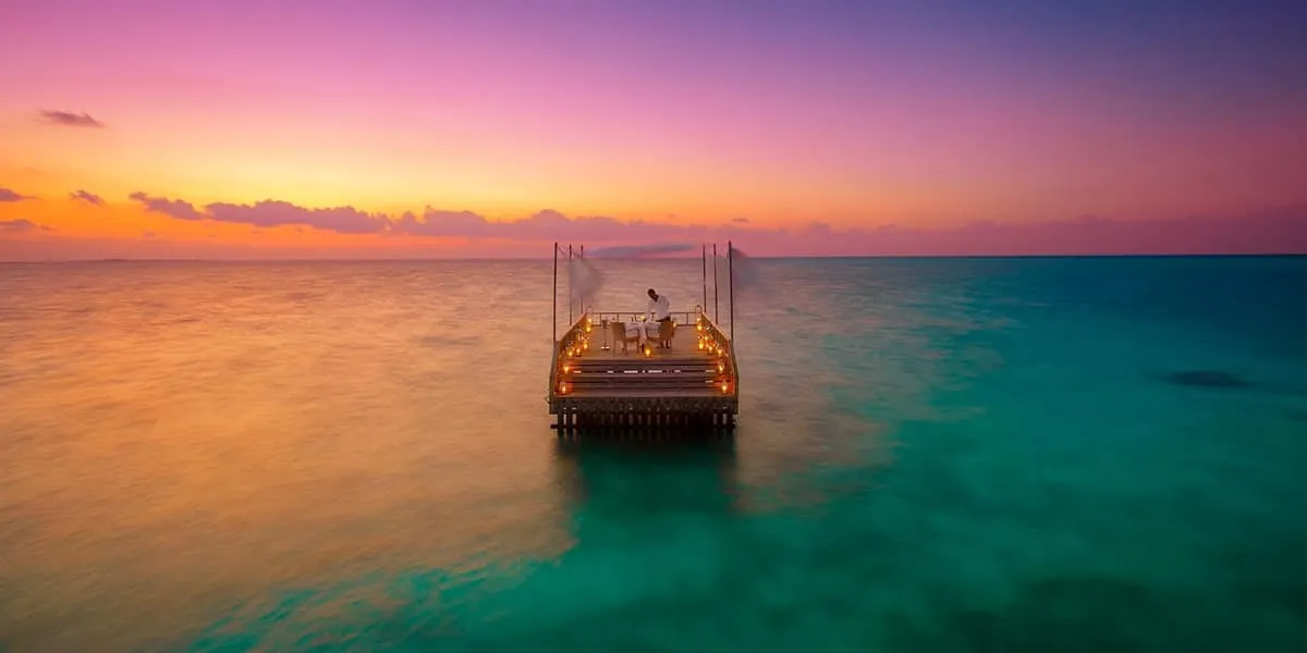 Lit dining platform on the sea at sunset under a pink and orange sky