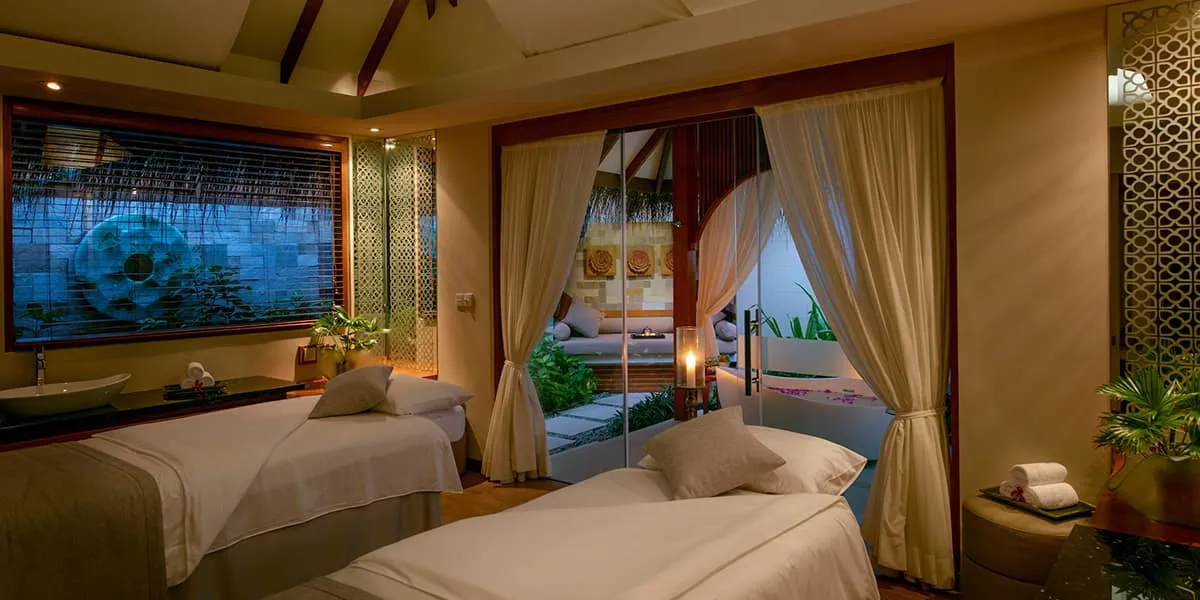Candlelit spa treatment room with massage beds and curtains