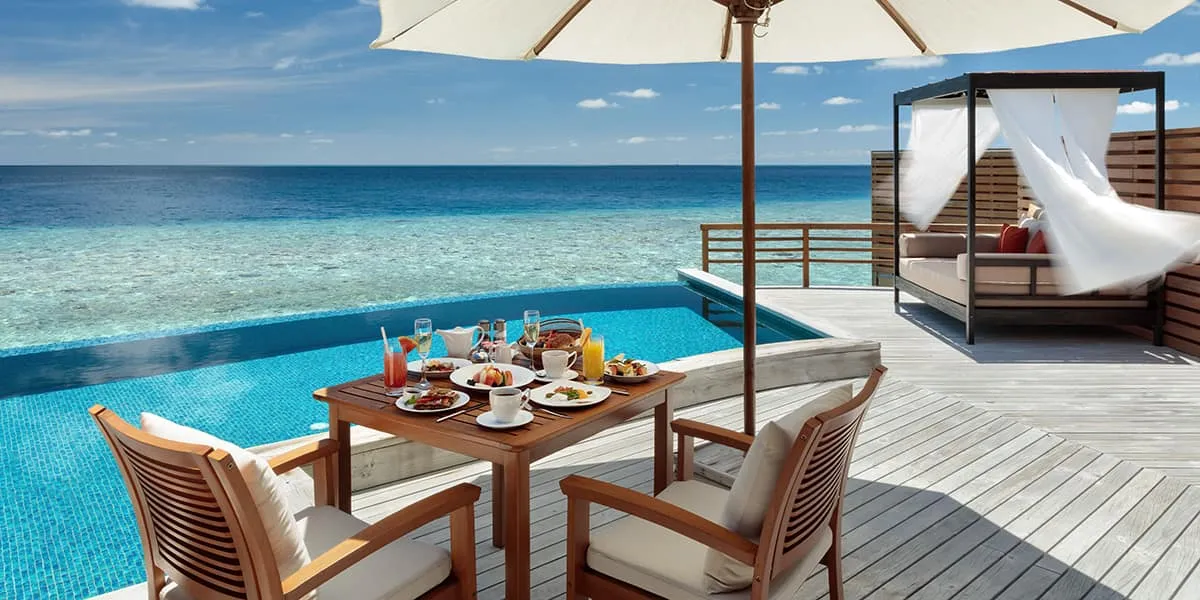 Breakfast table on a water villa deck beside an infinity pool and the lagoon