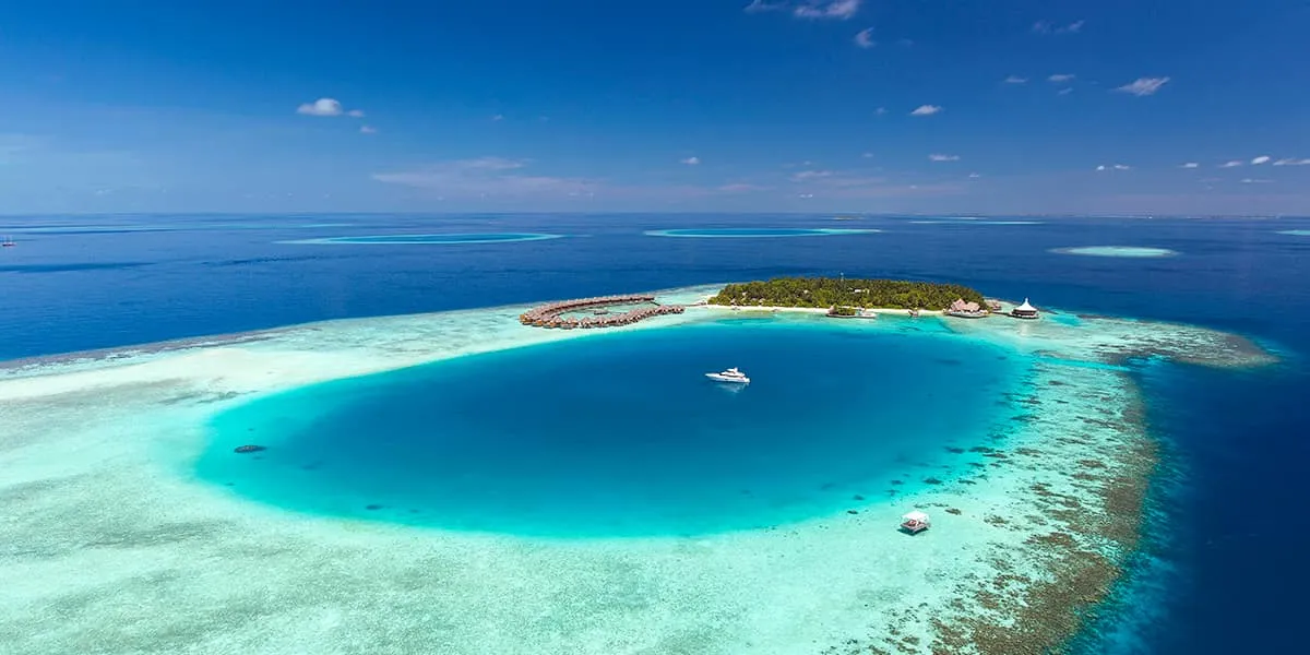 Aerial view of Baros island beside a deep blue lagoon ringed by coral reef