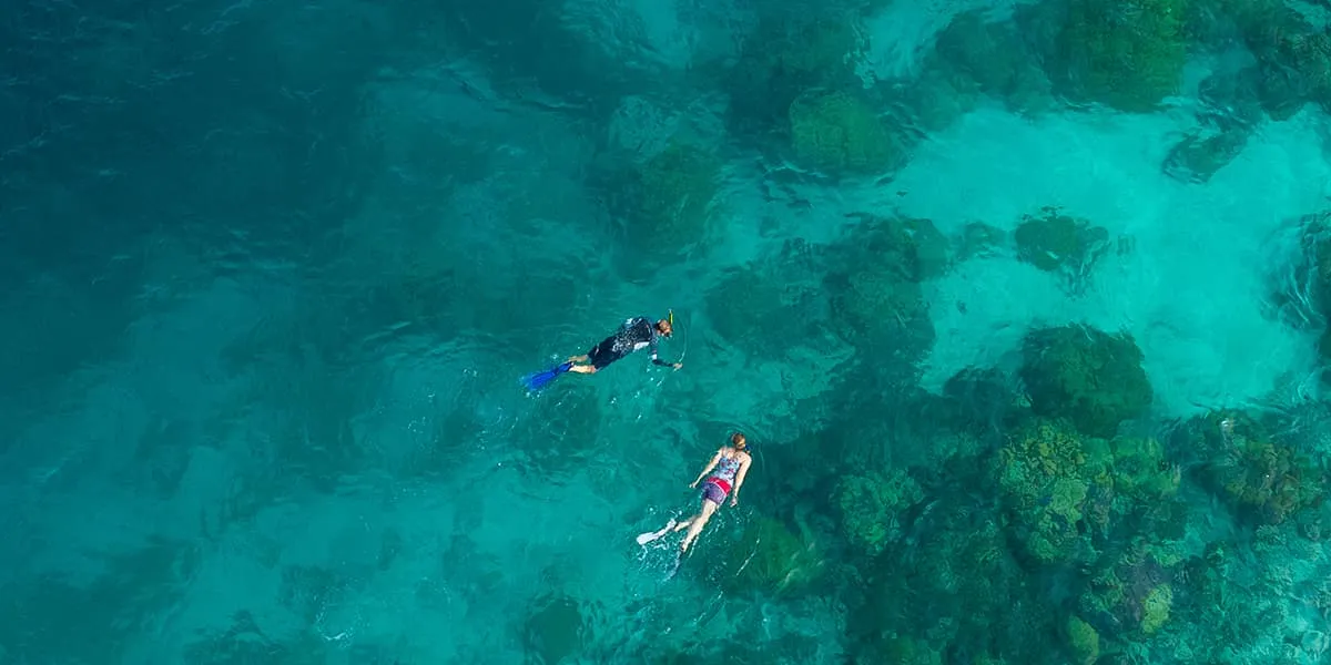 Aerial view of two snorkellers over coral patches in a turquoise lagoon