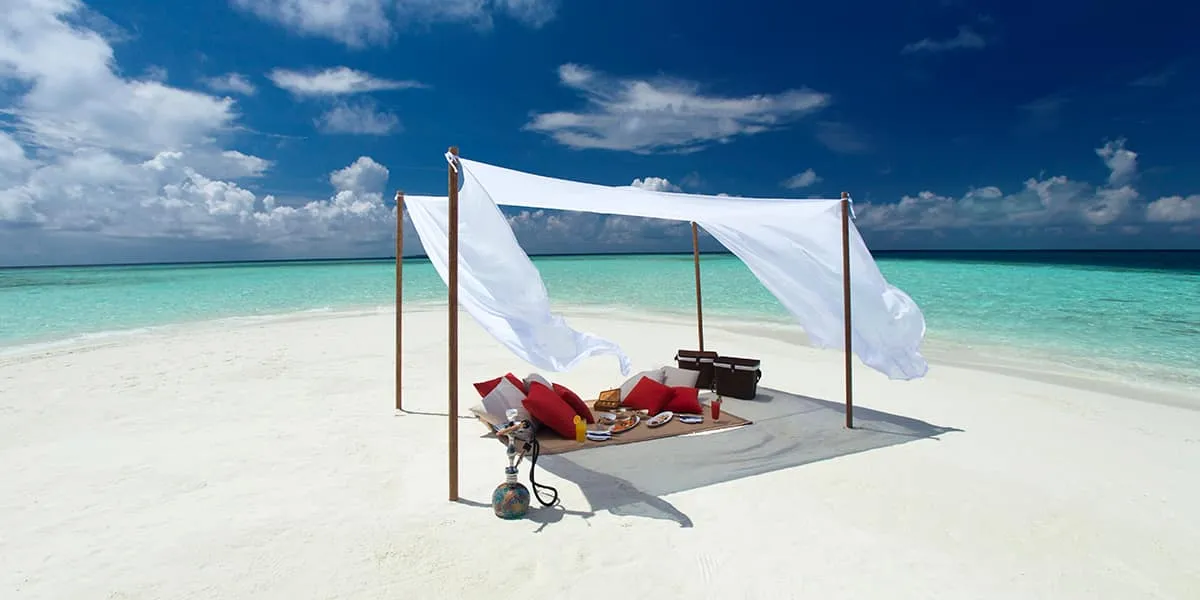 Sandbank picnic with cushions under a white canopy on a white-sand beach