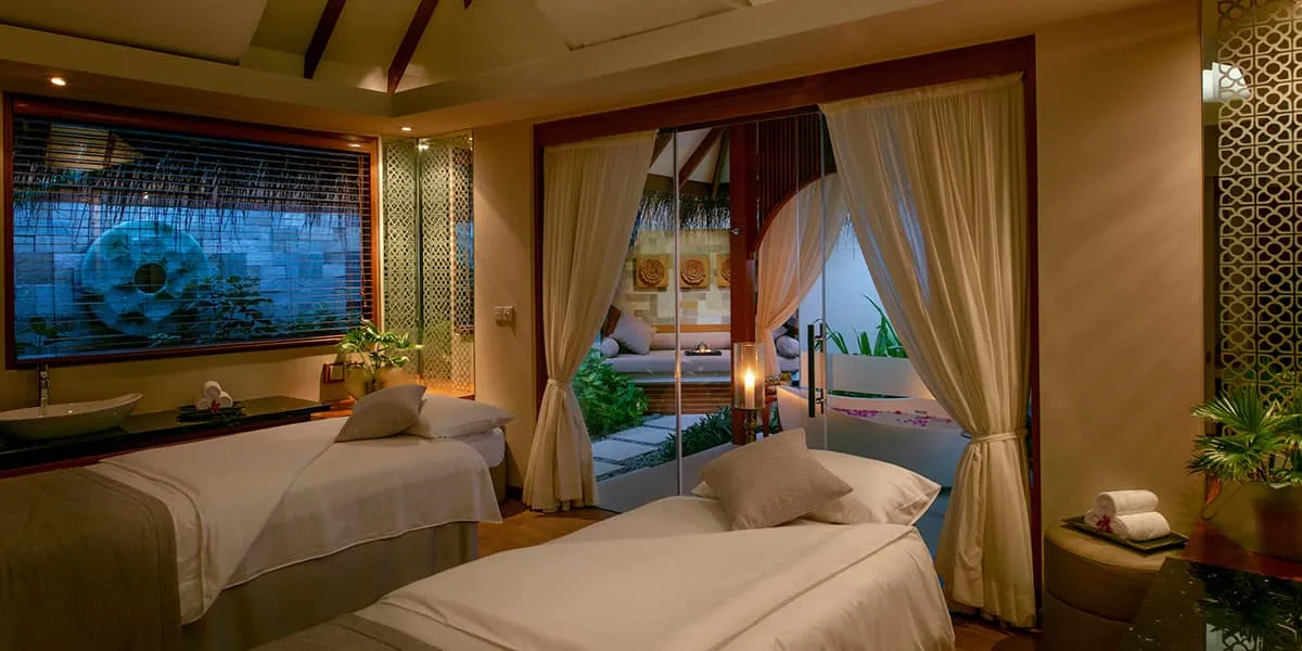 Candlelit spa treatment room with two massage beds and a lagoon-view window
